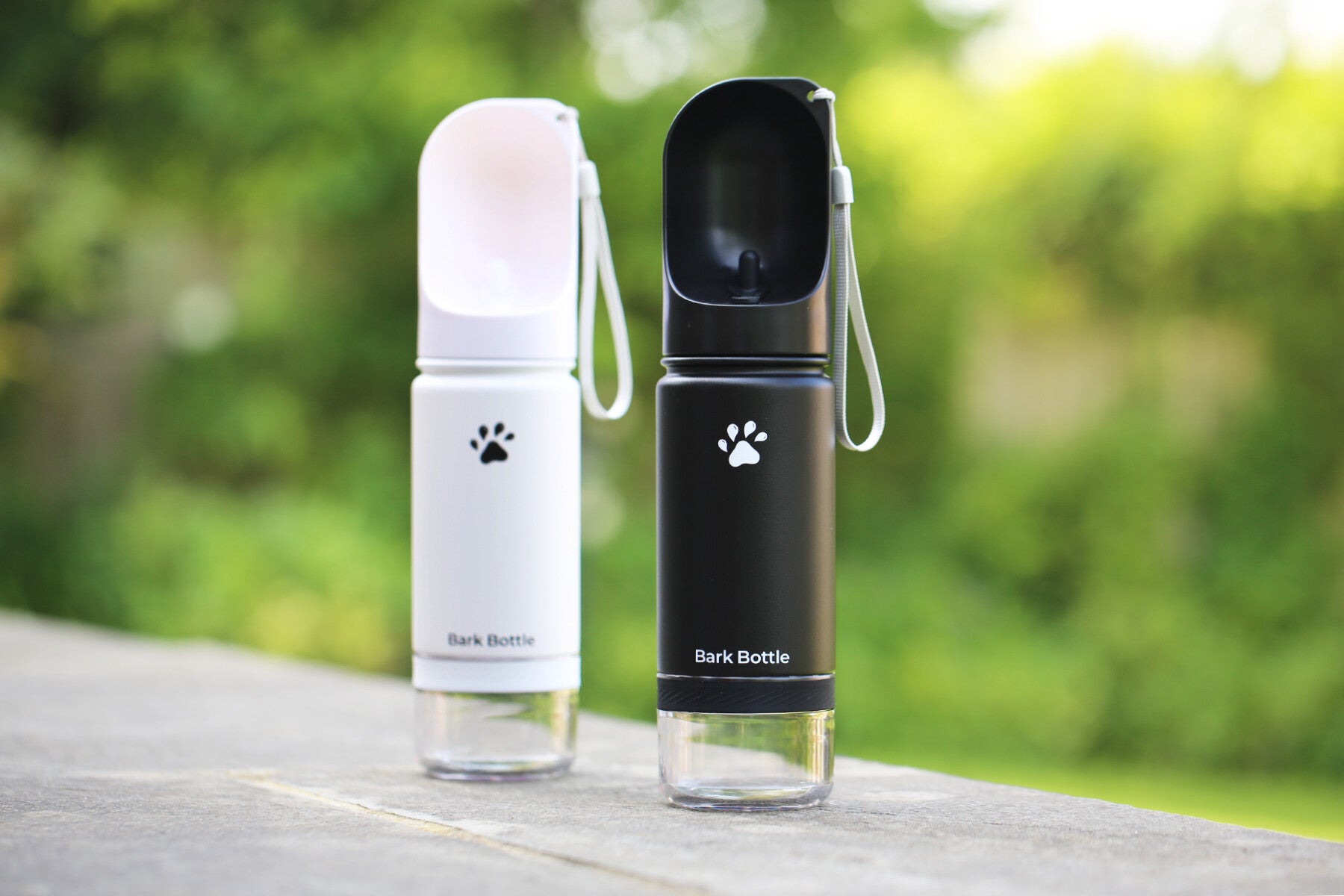 Two 'Bark Bottle' products, one white and one black, on a slate surface with a blurred green background.